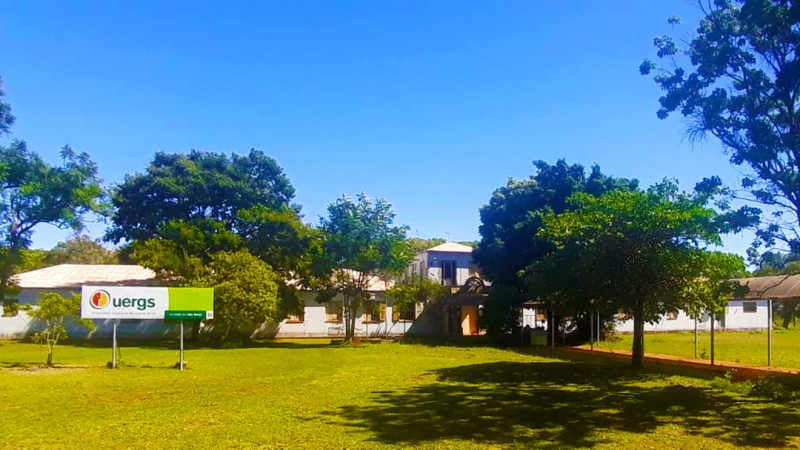 Amplo gramado à frente do prédio da Unidade, que está atrás de várias árvores. à esquerda, placa de identificação.