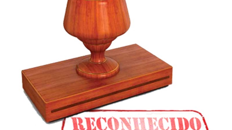 sobre fundo branco, carimbo de madeira à frente da palavra "reconhecido" escrita com letras vermelhas e borda da mesma cor com cantos arredondados.