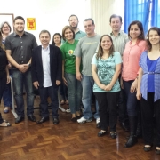 Grupo de pessoas sorridentes em pé, dentro de uma sala de aula.