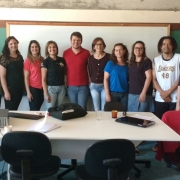 Grupo de pessoas sorridentes em pé, dentro de uma sala de aula.