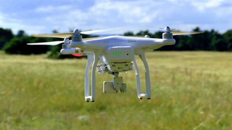Drone sobrevoando plantação. Acima, céu azul com algumas nuvens.
