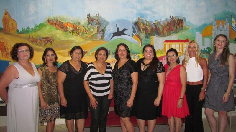 Nove mulheres posando para a foto. Ao centro, à esquerda, a prefeita e, à direita, a reitora. Ao fundo, painel com ilustrações diversas.