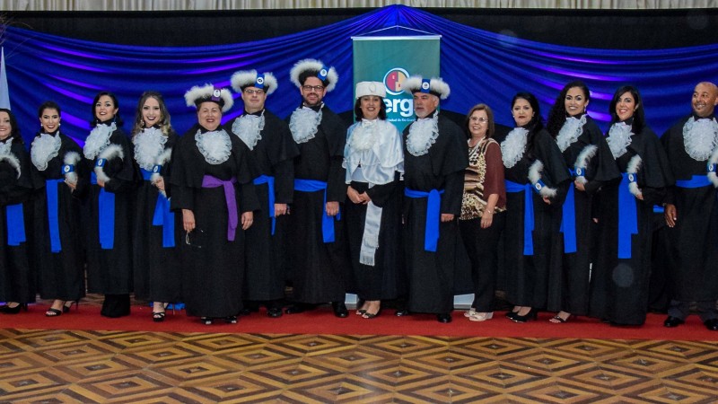 Turma de formandos vestindo toga, dispostos lados a lado, com as autoridades ao centro.