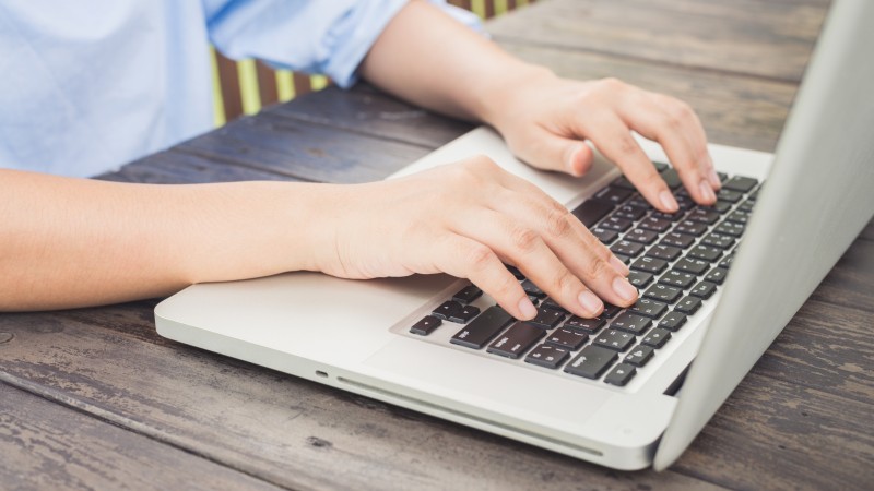 Close na mãos de um homem sobre o teclado de um notebook em cima de uma mesa.