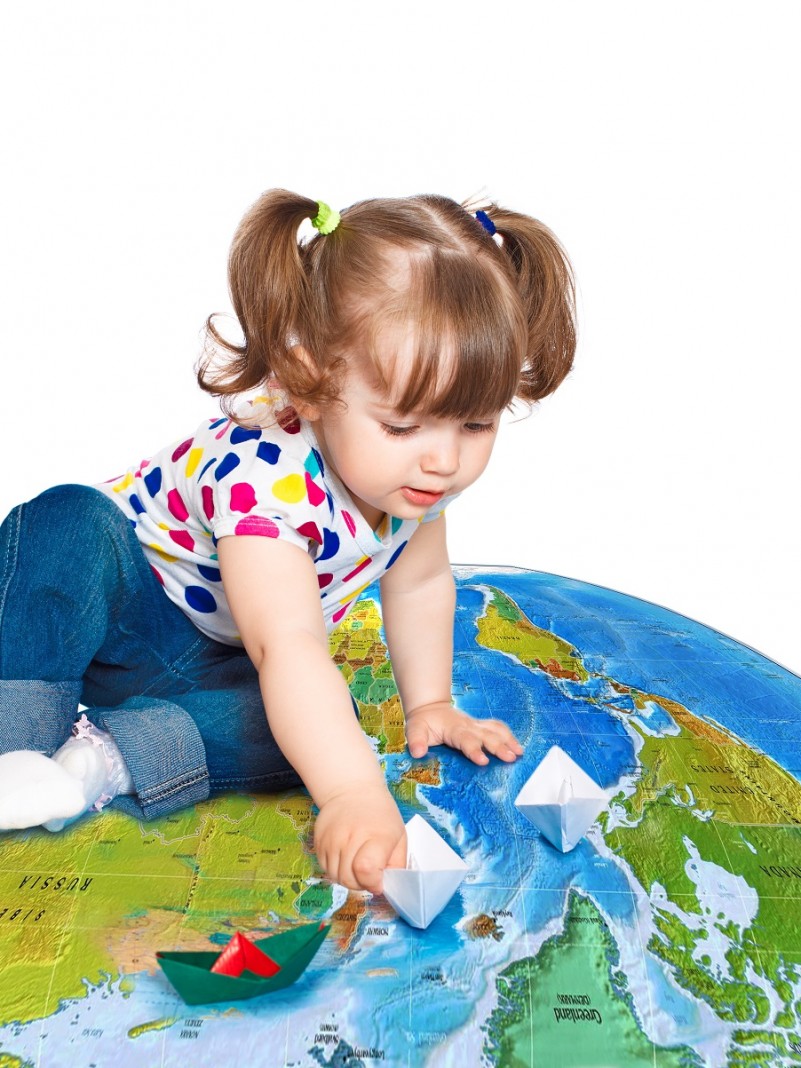 Menina brincando com barquinhos de papel sobre um globo com o mapa do mundo.