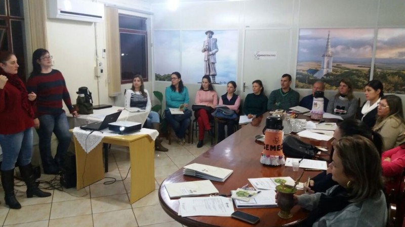 Diversas pessoas sentadas em círculo e outras atrás de uma mesa acompanham exposição sobre o curso.