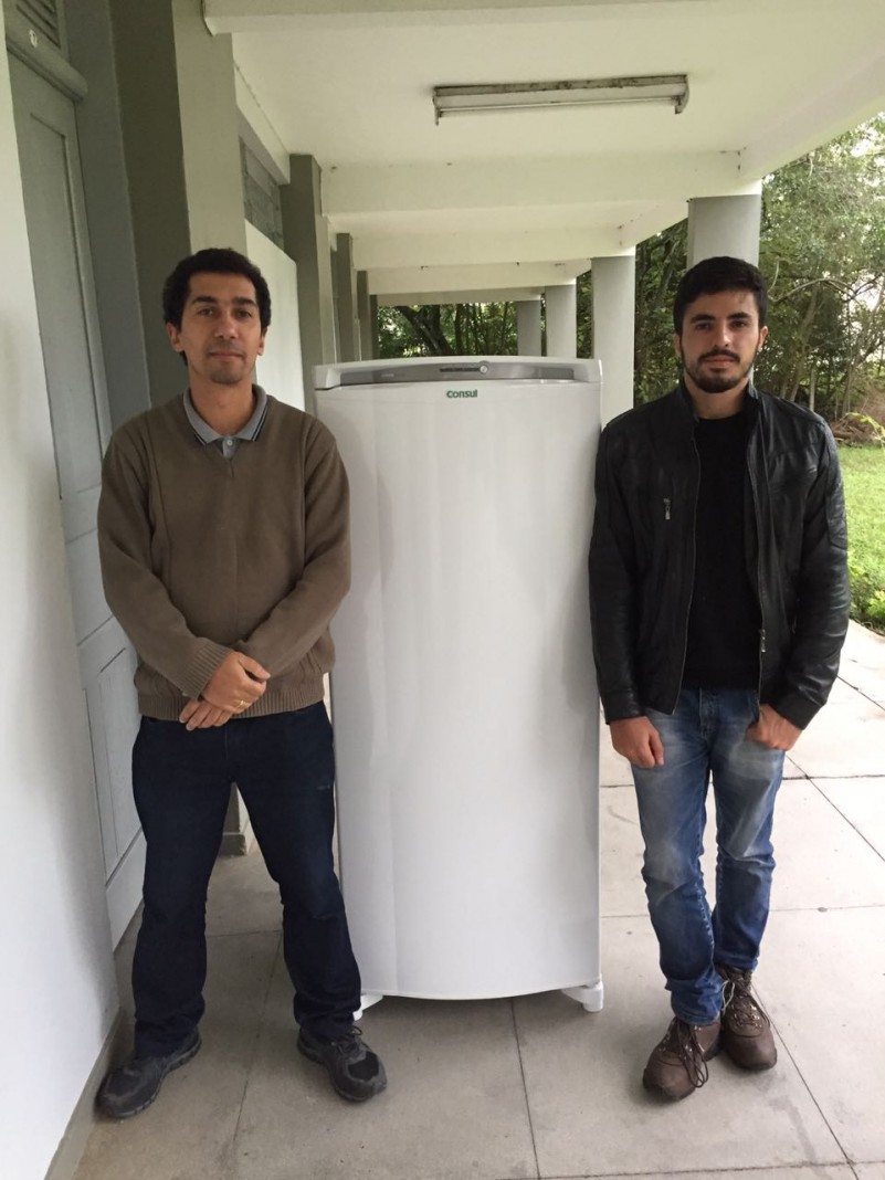 Presidente do Diretório Acadêmico e professor coordenador do curso posam ao lado da geladeira.
