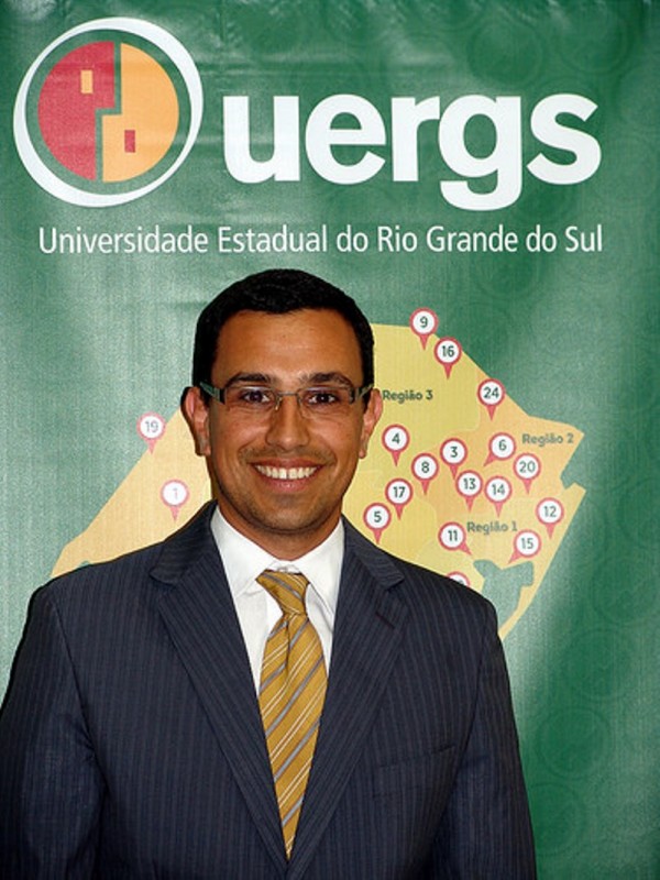 Homem sorridente de pele morena e cabelos pretos curtos. Usa óculos de grau.