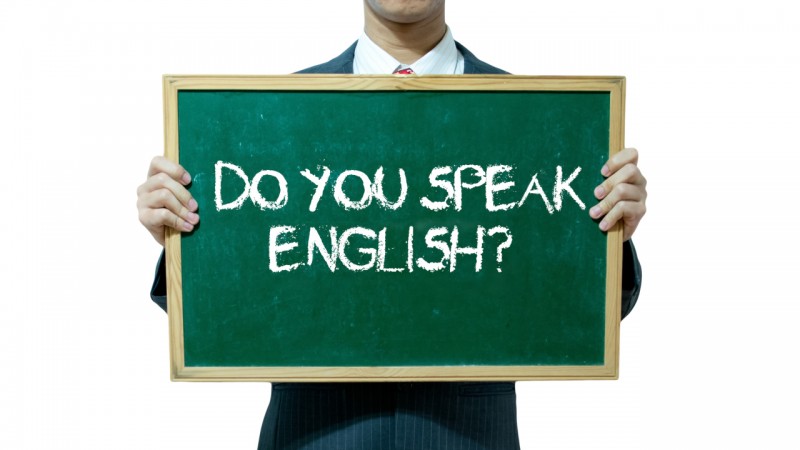 Recorte de um homem de terno segurando um quadro-negro com a escrita Do You Speak English?