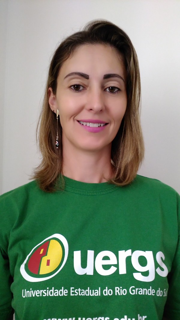 Mulher sorridente de pele clara, cabelos louros, lisos, na altura dos ombros. Usa camiseta verde com o logotipo da Uergs.