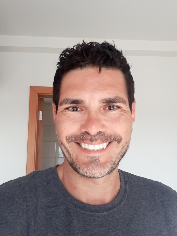 Homem de pele morena clara, olhos e cabelos curtos escuros, barba rla.