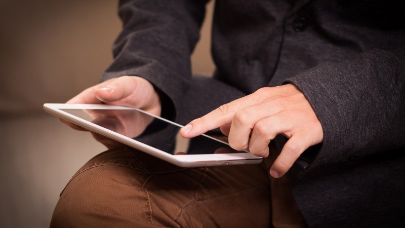 Rapas segura um tablet com a mão direita, enquanto clica na tecla com a mão esquerda.