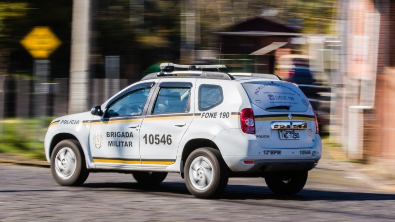 Foto colorida. Carro branco adesivado com a identificação da Brigada Militar, número da viatura 10546, fone 190. O fundo está desfocado.