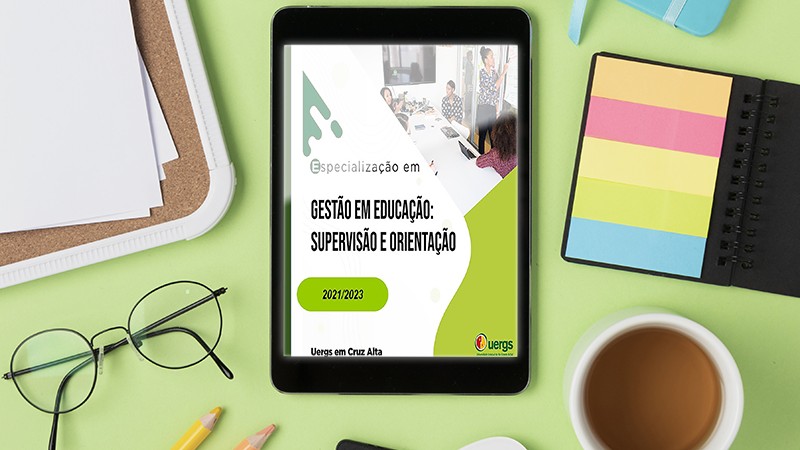 Imagem colorida. Tablet com a divulgação do evento na tela. ao redor, óculos de grau, xícara de café, folhas em branco e etiquetas coloridas.