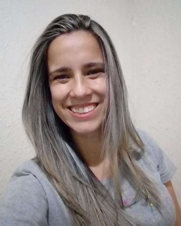 Mulher de pele morena clara, de cabelos longos em tom escuro com mechas loiras, com um grande sorriso.