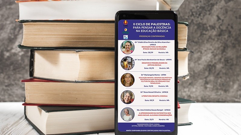 Foto colorida de smartphone apoiado em frente a uma pilha de livros. Na tela do smartphone, sobre fundo roxo, se lê II Ciclo de Palestras: Para pensar a docência na educação básica. Ao lado esquerdo, logotipos de realizadores. Na sequência, sobre fundo branco, fotos e informações de palestrantes. Sobre fundo roxo, link de transmissão.