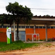 Ao fundo, pavilhão de tijolos à vista e um portão grande de entrada. À frente, o totem de identificação da Uergs à esquerda e placa da Uergs à direita.