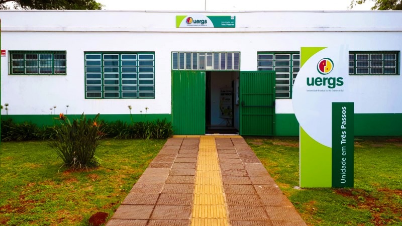 À direita, totem identificando a unidade. Ao fundo, prédio térreo da unidade, com um caminho centralizado.