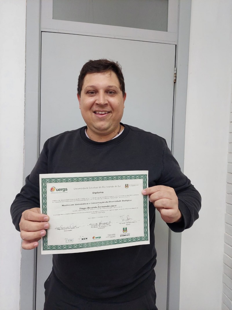 Homem sorridente vestindo blusa preta segura com as duas mãos um certificado.