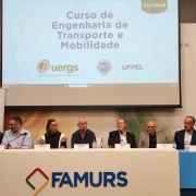 Foto colorida de pessoas sentadas atrás de uma mesa. Na mesa, lê-se Famurs. São sete pessoas sentadas. Elas são as autoridades do evento. Atrás e acima delas, há um telão com a identidade visual do evento.