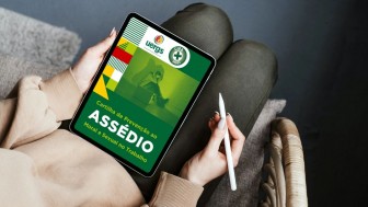 Fotografia de uma pessoa sentada com um tablet apoiado em seu colo e uma das mãos. A tela do dispositivo exibe a Cartilha de Prevenção ao Assédio Moral e Sexual no Trabalho. 