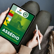 Fotografia de uma pessoa sentada com um tablet apoiado em seu colo e uma das mãos. A tela do dispositivo exibe a Cartilha de Prevenção ao Assédio Moral e Sexual no Trabalho. 